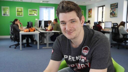 A photograph of Graeme Leighfield, Managing Director of GEL Studios, sat on a chair in an open plan office.