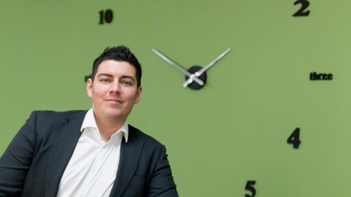 A photographo of Kyles Holmes, owner and MD of Black Nova Designs with a clock behind him