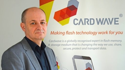 Paul Norbury, Chief Executive of Cardwave Services Ltd, sitting in front of a wall with the Cardwave logo on it.