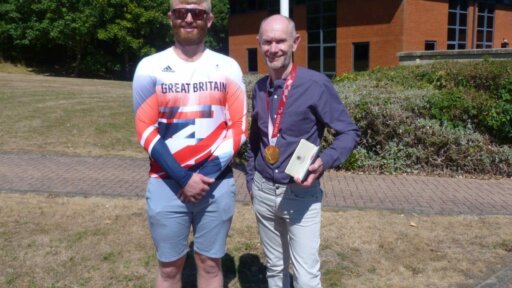 Paralympian, Chris Hunt Skelley MBE in his Team GB top standing next to Robin Deller, CEO of Imagine Cruising outside a building.