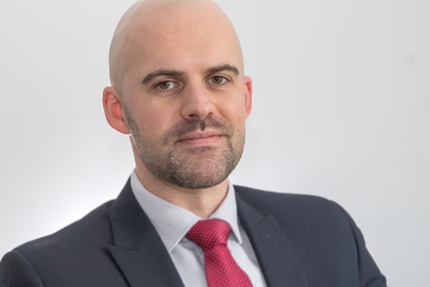 A head and shoulders photograph of Thrings Solicitor Richie Rees wearing a suit and a red tie, against a grey background.