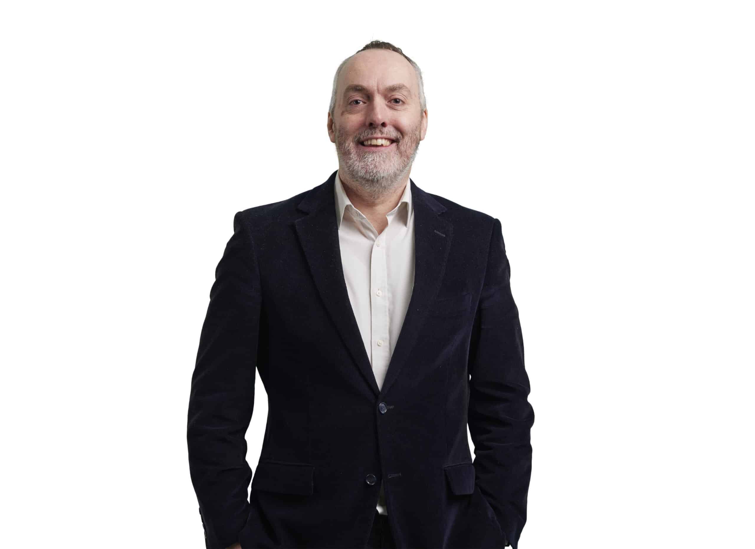 The photograph shows Steve Watson wearing a dark suit and white shirt, smiling against a white background