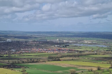 A photograph of the Wiltshire landscape taken from Westbury White Horse showing lots of green space, buildings and a blue sky with some clouds