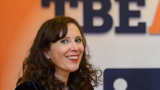 Anita Jaynes, Founder of The Business Exchange South West, smiling at a professional event with the TBE logo visible in the background. She is wearing a black outfit with a decorative brooch.