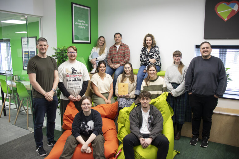 Photo of the Gel Studios team posing together in a bright creative workspace, with one member holding an engraved award, surrounded by colourful artwork and modern office décor.