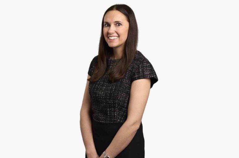 Professional portrait of lawyer Lucy Jones standing against a white background, wearing a black top and watch, with hands clasped in front.