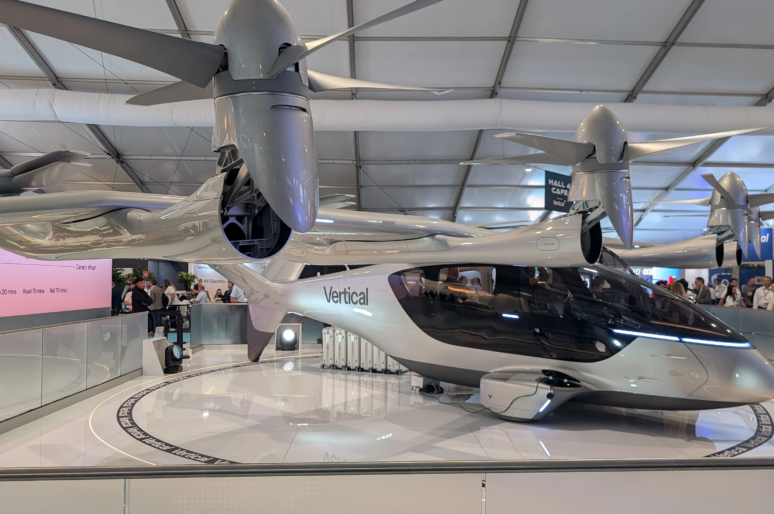 A sleek silver electric VTOL aircraft from Vertical Aerospace displayed inside an exhibition hall